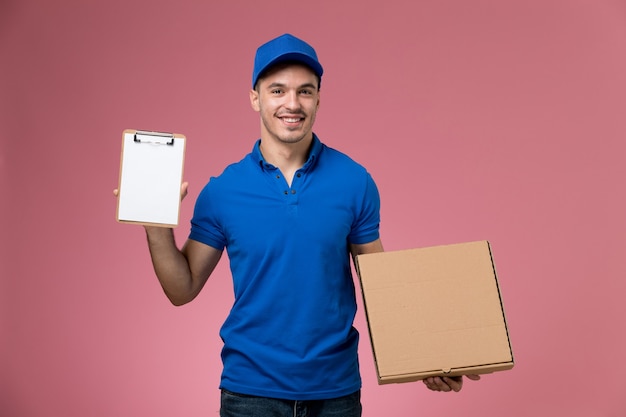 Mensajero masculino en uniforme azul con caja de comida y bloc de notas en rosa, entrega de trabajo de servicio uniforme