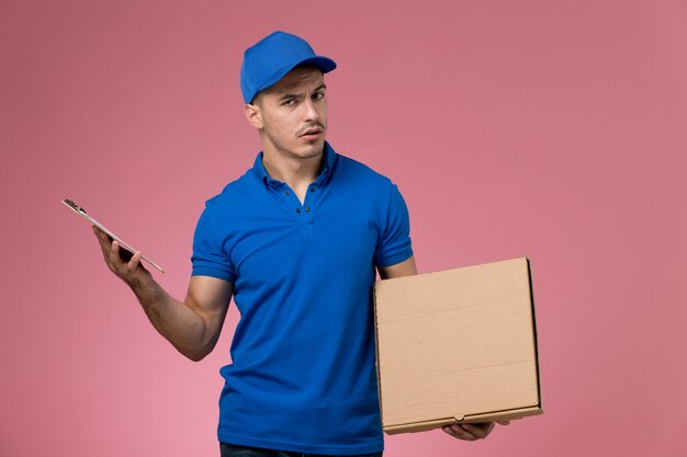 Mensajero masculino en uniforme azul con caja de comida y bloc de notas en rosa, trabajador de entrega de servicio uniforme de trabajo