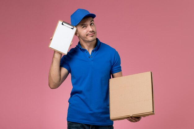 Mensajero masculino en uniforme azul con caja de comida de entrega y bloc de notas en rosa, servicio de trabajador de trabajo uniforme entrega