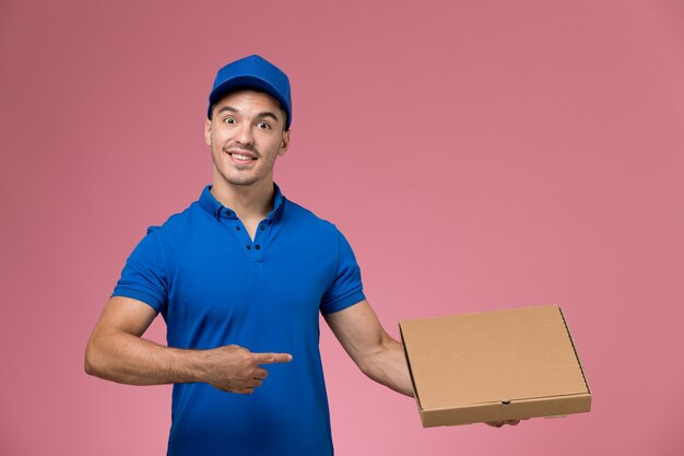 Mensajero masculino en uniforme azul con caja de entrega de comida sonriendo en rosa, servicio de entrega uniforme de trabajador de trabajo