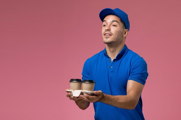 Mensajero masculino en uniforme azul entregando tazas de café en rosa, entrega de servicio uniforme de trabajador