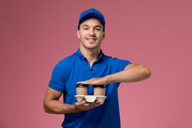 Mensajero masculino en uniforme azul entregando tazas de café en rosa, entrega de servicio uniforme de trabajador