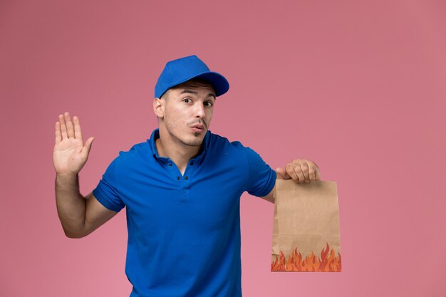 Mensajero masculino en uniforme azul con paquete de comida de entrega en rosa, servicio de entrega uniforme de trabajador de trabajo