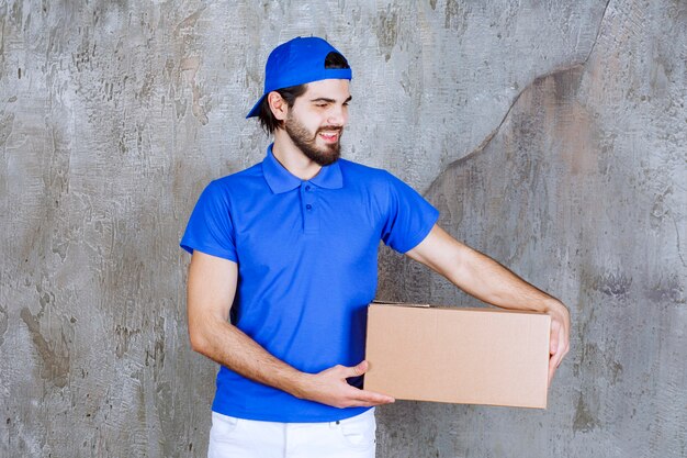 Mensajero masculino en uniforme azul que lleva una caja de cartón para llevar