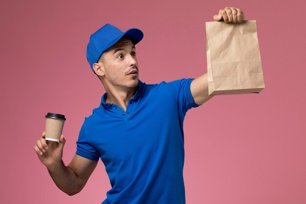 Mensajero masculino en uniforme azul que sostiene el paquete de comida de la taza de café de entrega en rosa, servicio de entrega uniforme del trabajador