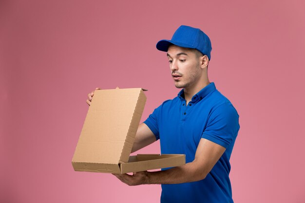 Mensajero masculino en uniforme azul sosteniendo y abriendo la caja de comida en rosa, servicio de entrega uniforme del trabajador de trabajo