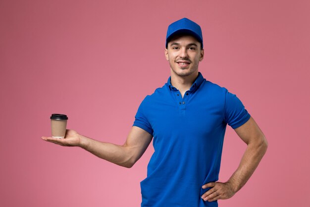 Mensajero masculino en uniforme azul sosteniendo la taza de café con una sonrisa en rosa, entrega de servicio uniforme de trabajador