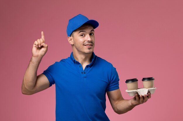 Mensajero masculino en uniforme azul sosteniendo tazas de café de entrega en rosa, servicio de trabajador de trabajo uniforme entrega