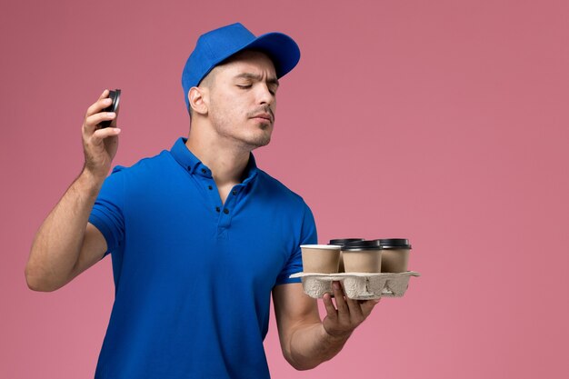 Mensajero masculino en uniforme azul sosteniendo tazas de café olerlas en rosa, trabajador de entrega de servicio uniforme