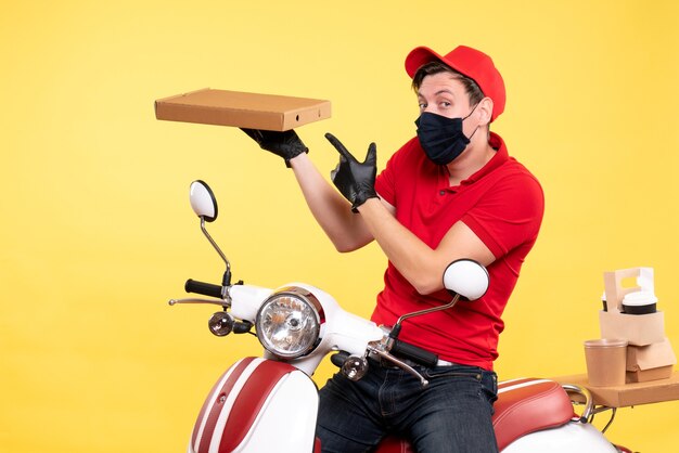 Mensajero masculino de vista frontal en bicicleta en máscara con caja de comida en amarillo