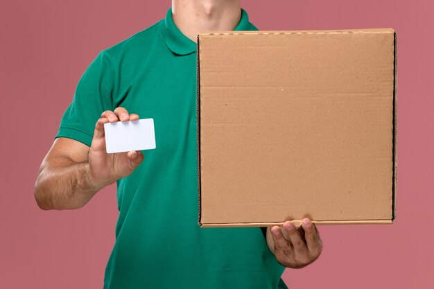 Mensajero masculino de vista frontal cercana en uniforme verde con caja de comida con tarjeta blanca sobre fondo rosa