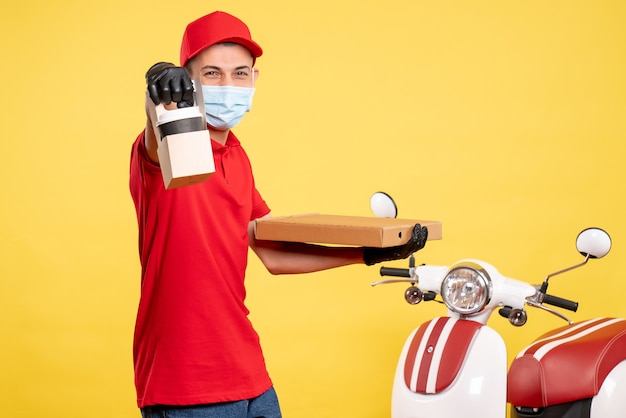 Mensajero masculino de vista frontal con entrega de café y caja en amarillo servicio de trabajo covid- virus uniforme de bicicleta de color