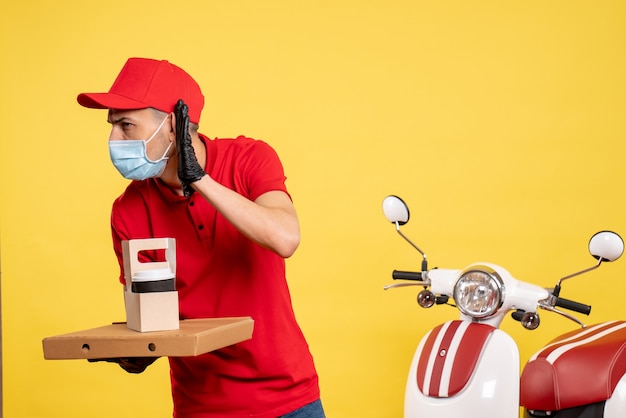 Mensajero masculino de vista frontal en máscara con entrega de café y caja en amarillo trabajo covid- color virus pandemia uniforme de trabajo