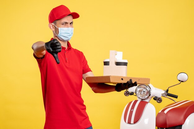 Mensajero masculino de vista frontal en máscara con entrega de café y caja en trabajo de servicio amarillo covid- virus de color pandémico uniforme