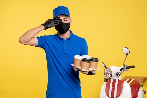 Foto gratuita mensajero masculino de vista frontal en máscara negra sosteniendo café en amarillo trabajo covid- uniforme de entrega de servicios pandémicos