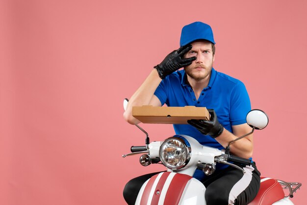 Mensajero masculino de vista frontal sentado en bicicleta y sosteniendo la caja de pizza en el rosa