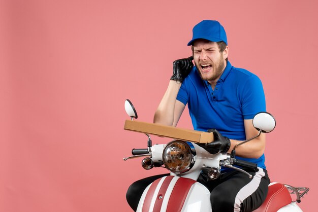 Foto gratuita mensajero masculino de vista frontal sentado en bicicleta y sosteniendo la caja de pizza en el rosa