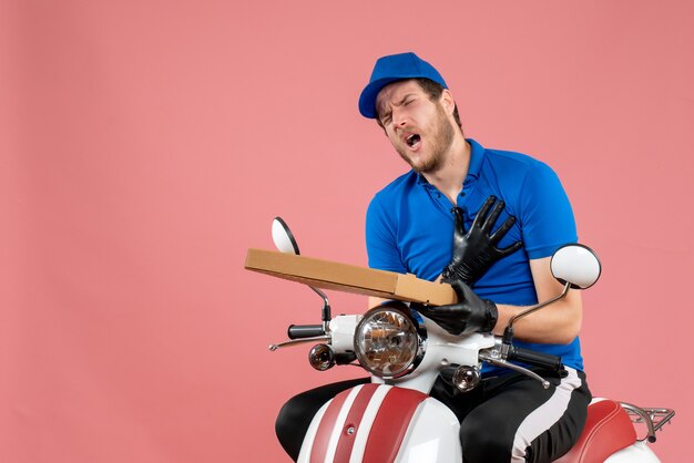 Mensajero masculino de vista frontal sentado en bicicleta y sosteniendo la caja de pizza en el rosa