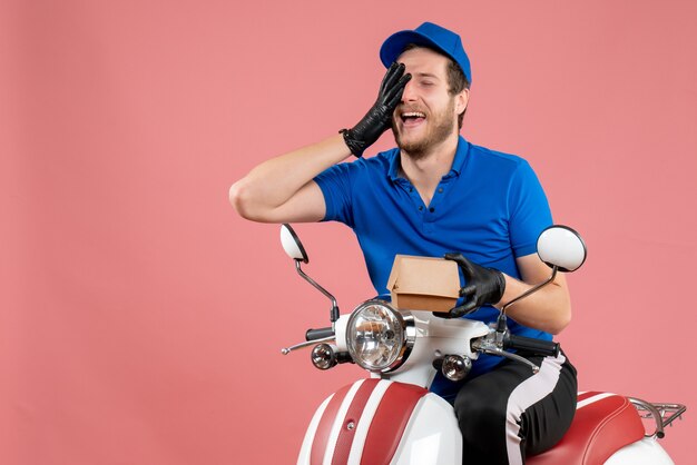 Mensajero masculino de vista frontal sentado en bicicleta y sosteniendo un pequeño paquete de comida en rosa