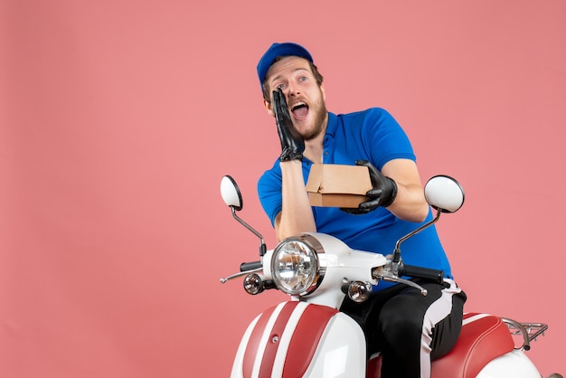 Mensajero masculino de vista frontal sentado en bicicleta y sosteniendo un pequeño paquete de comida en rosa