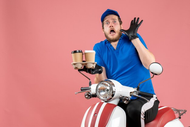 Mensajero masculino de vista frontal sentado en bicicleta y sosteniendo tazas de café en el rosa