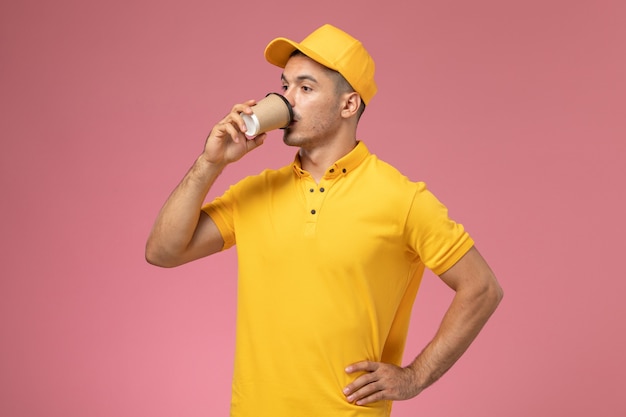 Foto gratuita mensajero masculino de vista frontal en uniforme amarillo bebiendo café sobre fondo rosa