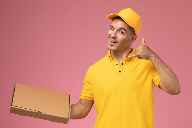 Mensajero masculino de vista frontal en uniforme amarillo con caja de entrega de alimentos en el escritorio rosa