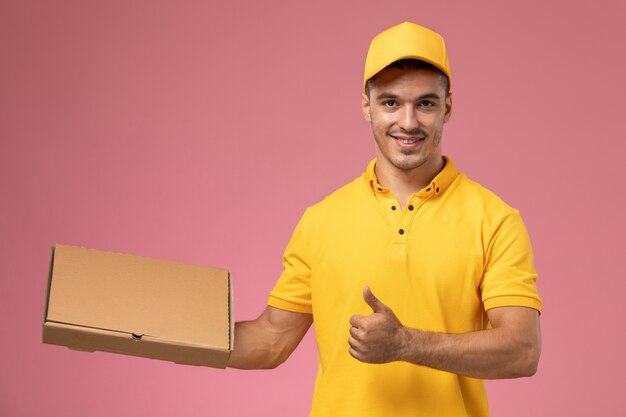 Mensajero masculino de vista frontal en uniforme amarillo con caja de entrega de alimentos en el fondo rosa