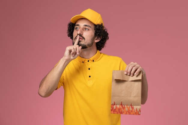 Mensajero masculino de vista frontal en uniforme amarillo con paquete de comida de papel en la pared rosa claro