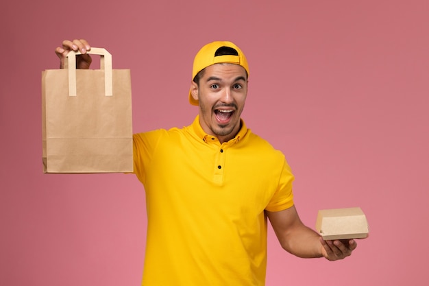 Mensajero masculino de vista frontal en uniforme amarillo con paquetes de comida de entrega en el fondo rosa claro.