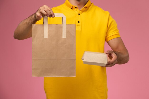 Mensajero masculino de vista frontal en uniforme amarillo con paquetes de comida de entrega en el fondo rosa claro.