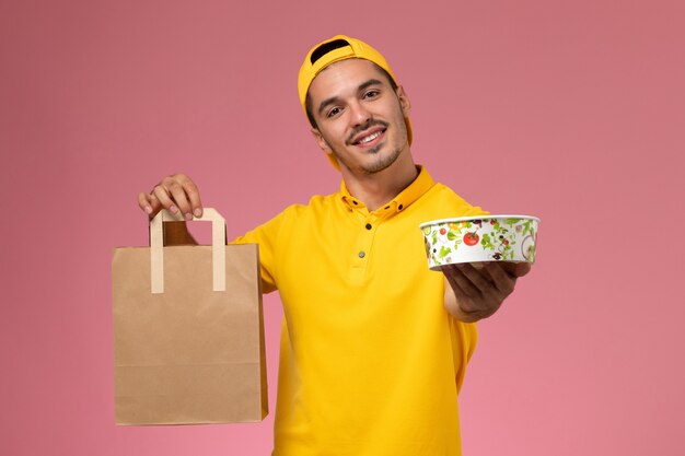 Mensajero masculino de la vista frontal en uniforme amarillo que sostiene el cuenco del paquete de alimentos de entrega sobre fondo rosa.