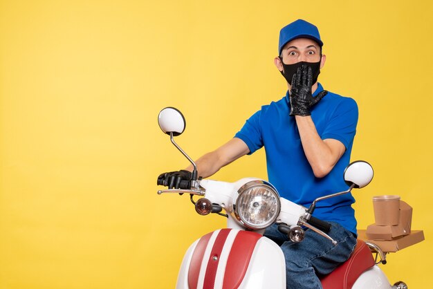 Mensajero masculino de vista frontal en uniforme azul y máscara en amarillo trabajo covid- entrega pandemia virus de trabajo en bicicleta