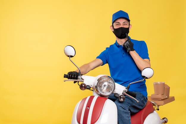 Mensajero masculino de vista frontal en uniforme azul y máscara en bicicleta amarilla covid- trabajo de servicio de virus de trabajo de entrega pandémica