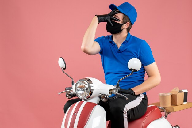 Mensajero masculino de vista frontal en uniforme azul y máscara en servicio de comida rápida de virus rosa trabajo en bicicleta covid- trabajo de entrega