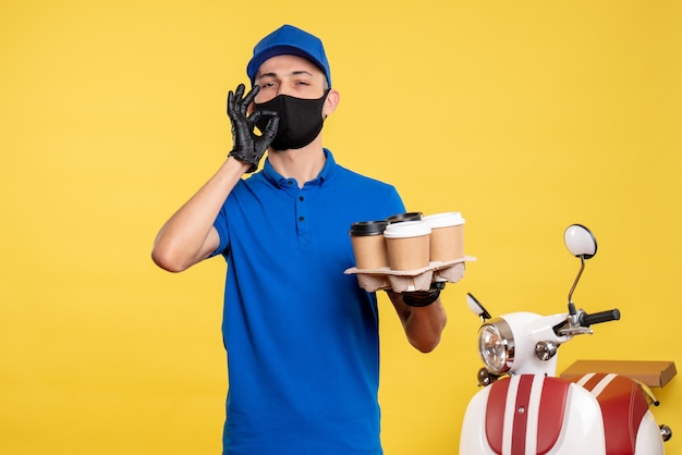 Foto gratuita mensajero masculino de vista frontal en uniforme azul y máscara sosteniendo café en el servicio de trabajo uniforme amarillo covid- pandemia de entrega de trabajo