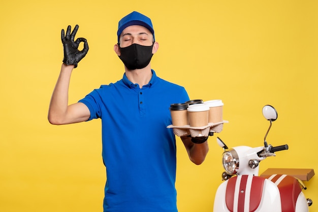 Foto gratuita mensajero masculino de vista frontal en uniforme azul y máscara sosteniendo café en el servicio de trabajo uniforme amarillo covid- pandemia de entrega de trabajo