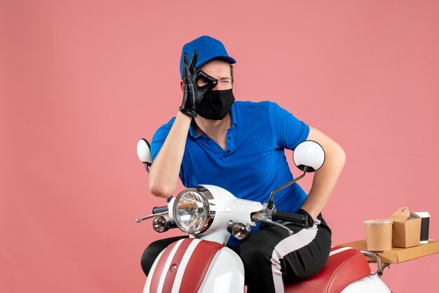 Mensajero masculino de vista frontal en uniforme azul y máscara en trabajo rosa servicio de comida rápida trabajo en bicicleta covid- virus alimentario