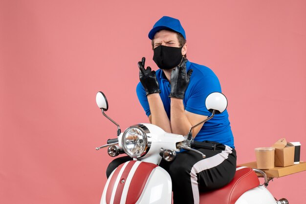 Mensajero masculino de vista frontal en uniforme azul y máscara en el virus de entrega rosa servicio de comida rápida de comida trabajo en bicicleta covid- trabajo