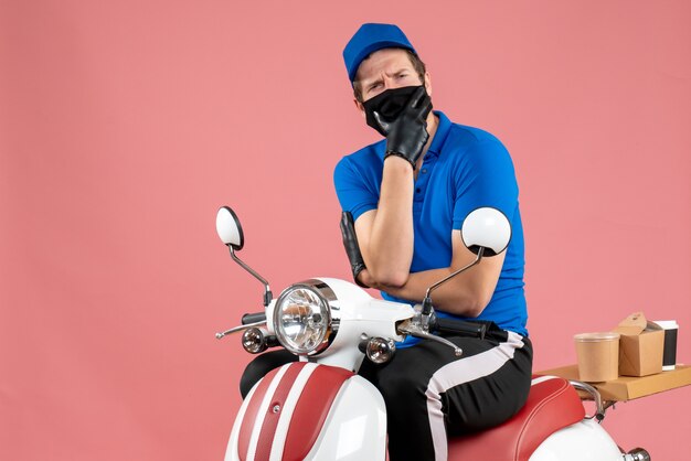 Mensajero masculino de vista frontal en uniforme azul y máscara en el virus de entrega rosa servicio de comida rápida de comida trabajo en bicicleta covid- trabajo