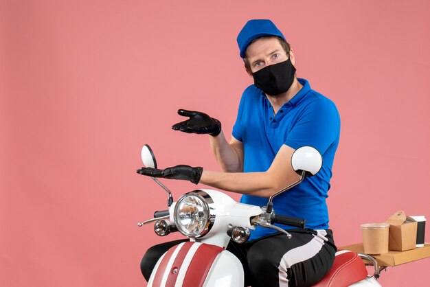 Mensajero masculino de vista frontal en uniforme azul y máscara en el virus rosa entrega de trabajo en bicicleta trabajo de servicio covid de comida rápida