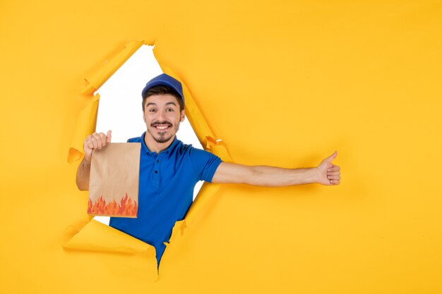 Mensajero masculino de vista frontal en uniforme azul con paquete de alimentos en el espacio amarillo