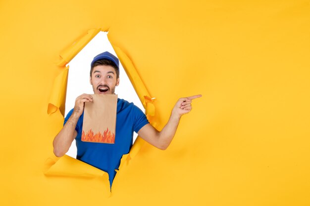 Foto gratuita mensajero masculino de vista frontal en uniforme azul con paquete de alimentos en el espacio amarillo