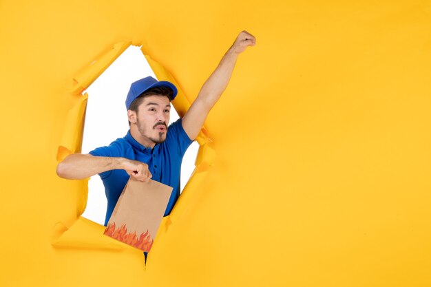 Mensajero masculino de vista frontal en uniforme azul sosteniendo el paquete de alimentos en el espacio amarillo