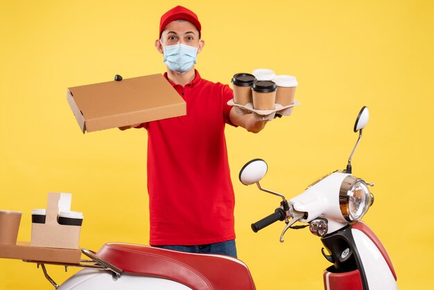 Mensajero masculino de vista frontal en uniforme con caja de café y comida en el color amarillo del virus del trabajo uniforme del covid del servicio pandémico amarillo