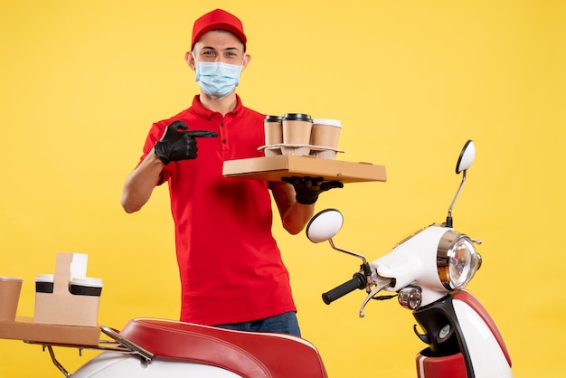 Foto gratuita mensajero masculino de vista frontal en uniforme con caja de café y comida en el servicio pandémico amarillo trabajo de virus de trabajo uniforme de covid