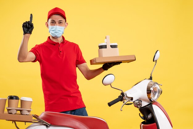 Mensajero masculino de vista frontal en uniforme rojo con caja de comida y café en trabajo de trabajo uniforme de virus covid pandémico de color amarillo