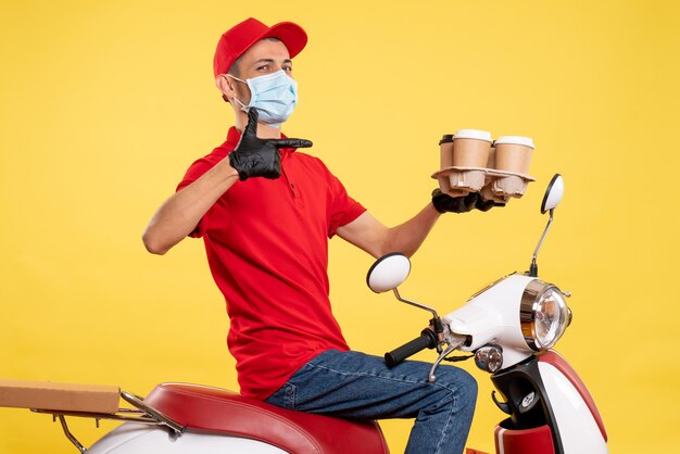 Mensajero masculino de vista frontal en uniforme rojo y máscara con café en color amarillo trabajo pandemia covid- virus de servicio de alimentos