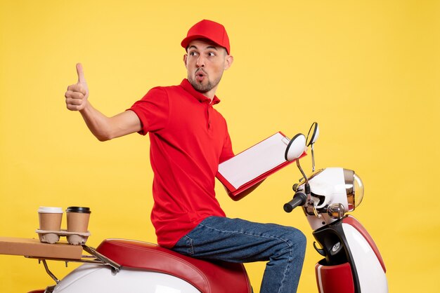 Mensajero masculino de vista frontal en uniforme rojo con nota de archivo en el trabajo de servicio de trabajador de entrega de color de bicicleta amarilla