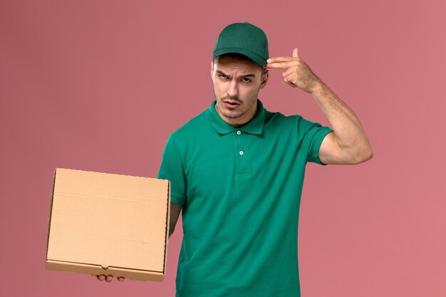 Mensajero masculino de vista frontal en uniforme verde con caja de comida en el fondo rosa